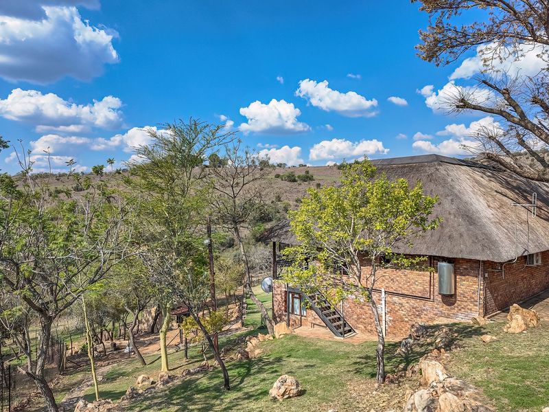 Rear view of a face brick house featuring a traditional thatch roof, external staircase, and surrounding natural landscape.