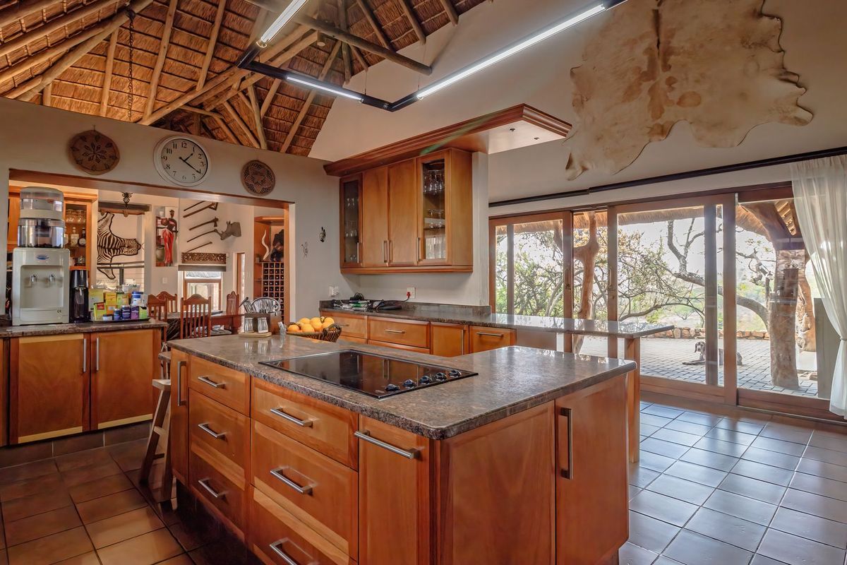 Spacious kitchen featuring a central island with cooktop, wooden cabinetry, stone countertops, and a high vaulted thatched ceiling with direct access to the patio.