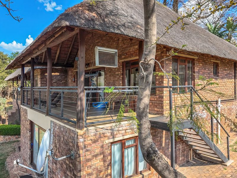 Rear view of a rustic brick house featuring a traditional thatch roof, a covered balcony with metal railings, and an external staircase.