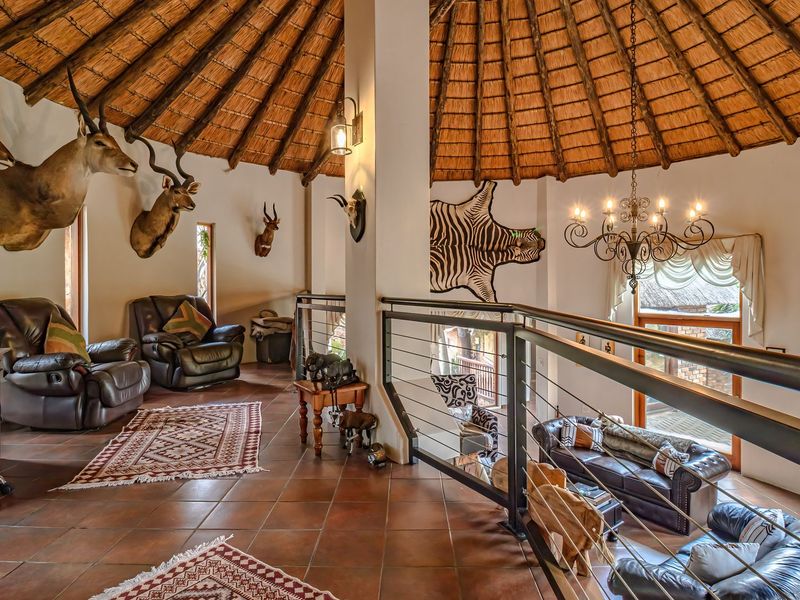 Spacious mezzanine living area featuring a high thatched roof with exposed timber rafters, terracotta flooring, and a decorative wrought iron chandelier.