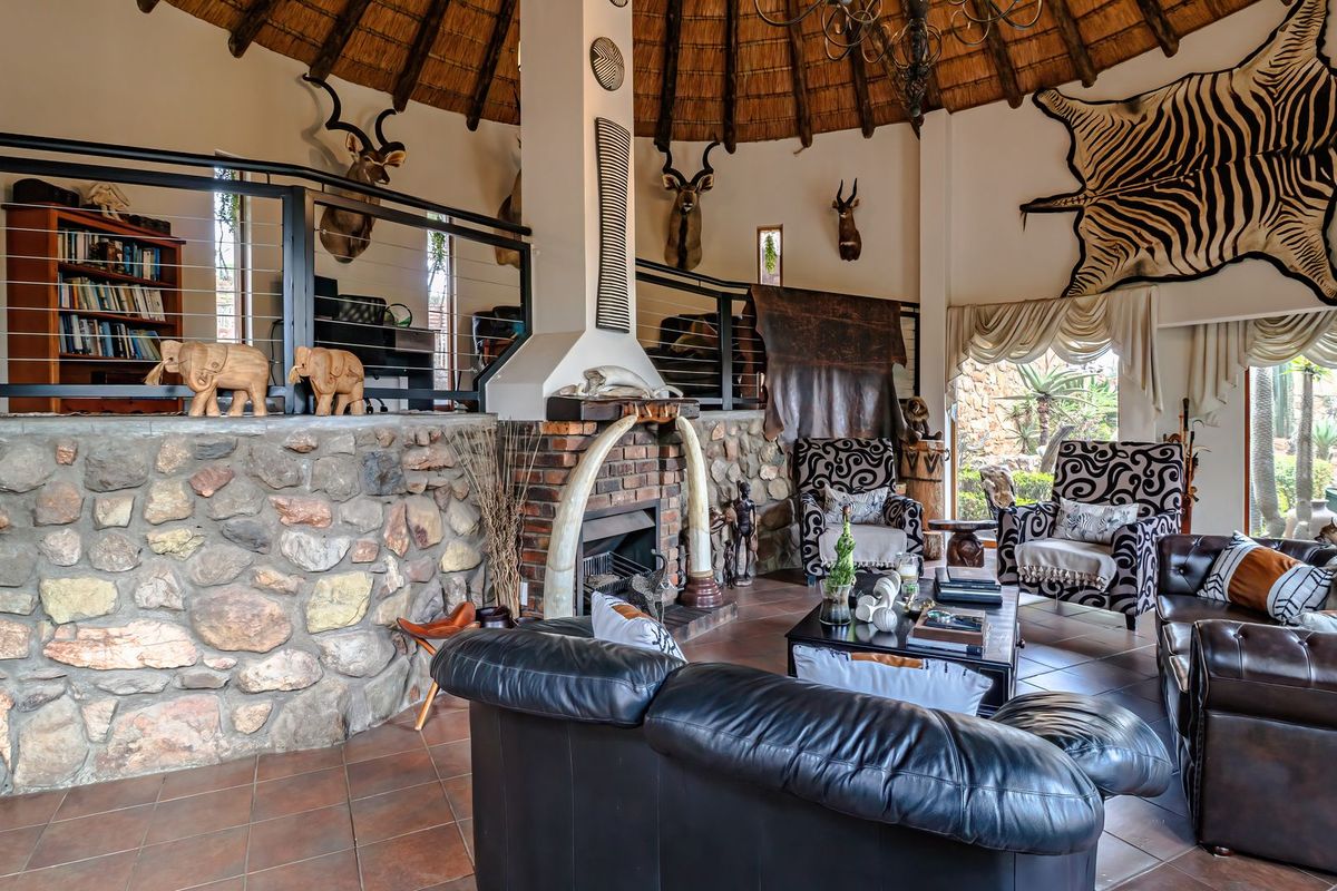 Spacious living room featuring a high thatched ceiling, stone-clad feature wall, and a central brick fireplace, with an elevated mezzanine level overlooking the area.