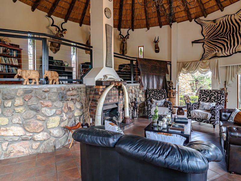 Spacious living room featuring a high thatched ceiling, stone-clad feature wall, and a central brick fireplace, with an elevated mezzanine level overlooking the area.