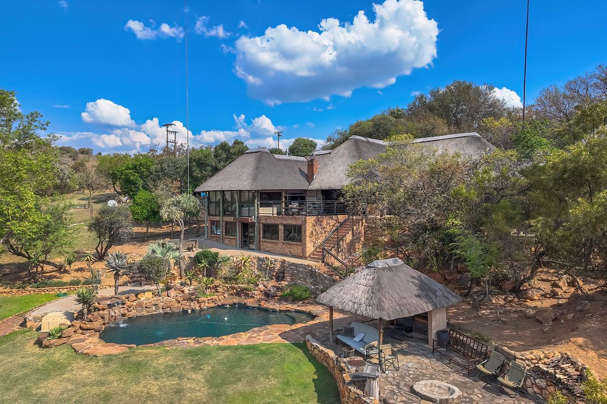 Aerial view of a multi-level residence featuring a thatched roof, stone-surrounded swimming pool, and a landscaped garden with a thatched gazebo.