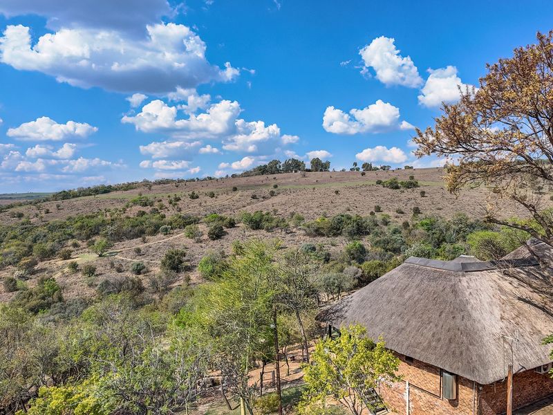 Elevated view overlooking a vast natural landscape with a traditional thatched-roof structure visible in the foreground.