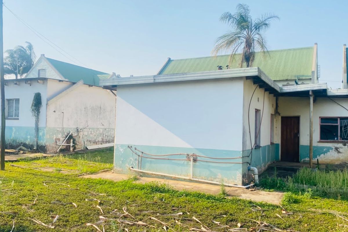 Rear view of the property showing exterior walls with peeling paint, exposed plumbing, and a corrugated metal roof structure.