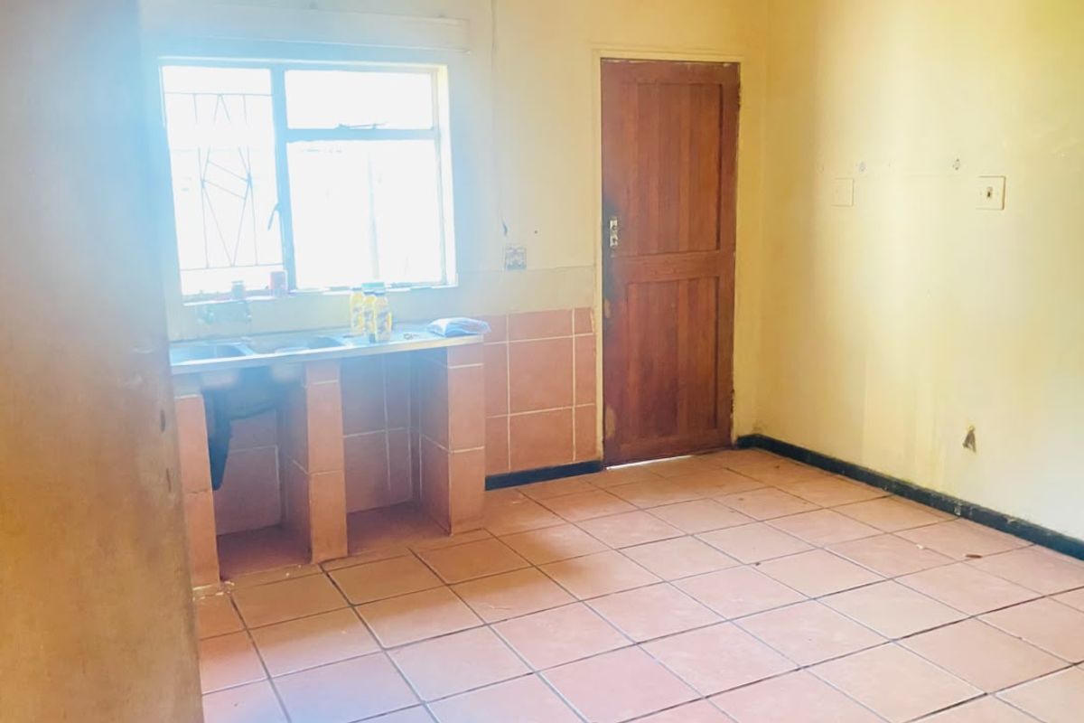 A basic, empty kitchen area featuring tiled flooring, a built-in sink unit, and a timber door, offering a blank canvas for renovation.