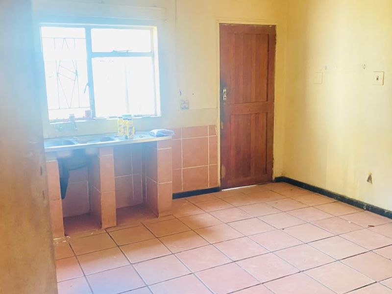 A basic, empty kitchen area featuring tiled flooring, a built-in sink unit, and a timber door, offering a blank canvas for renovation.