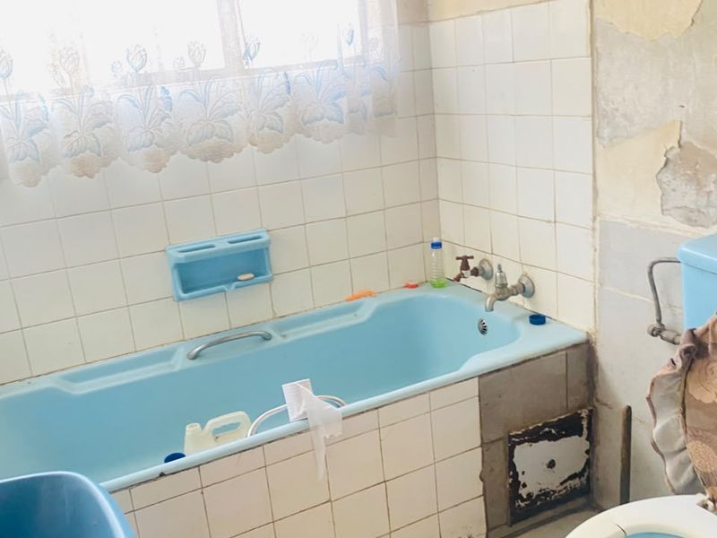 A dated bathroom featuring a blue bathtub and toilet, requiring significant renovation due to damaged wall finishes and worn tiling.