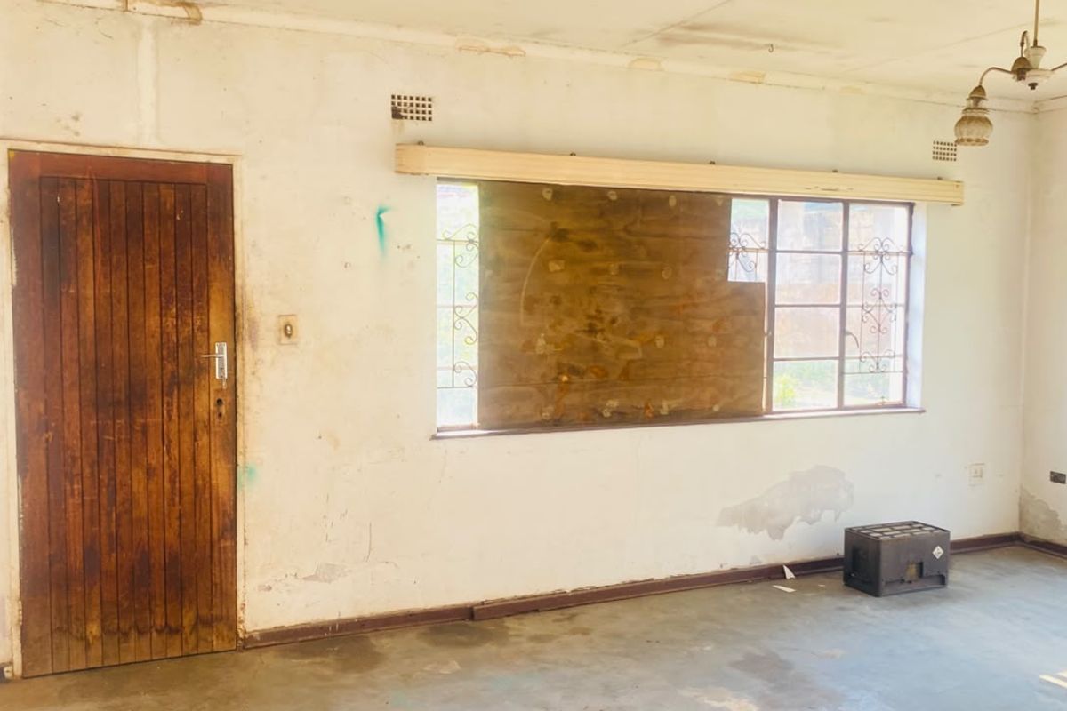 An empty living room requiring significant renovation, featuring original timber doors, steel windows with security bars, and visible wear to walls and ceiling finishes.