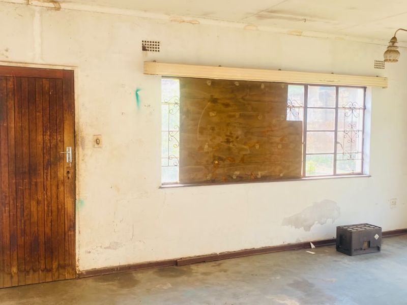 An empty living room requiring significant renovation, featuring original timber doors, steel windows with security bars, and visible wear to walls and ceiling finishes.