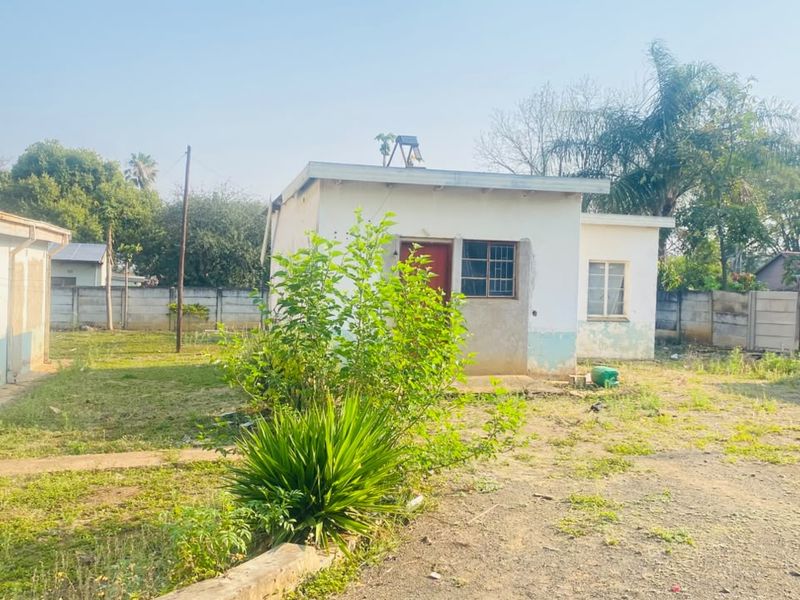 Rear view of the property showing a detached structure, precast boundary walls, and a large garden area requiring landscaping and exterior maintenance.