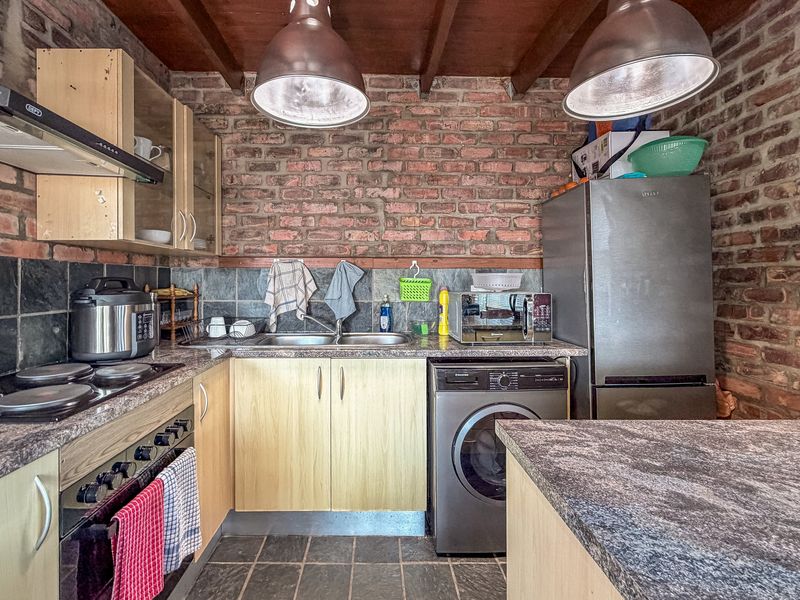 A rustic kitchen featuring exposed brick walls, slate tile flooring, timber ceiling beams, and functional cabinetry with integrated appliances.