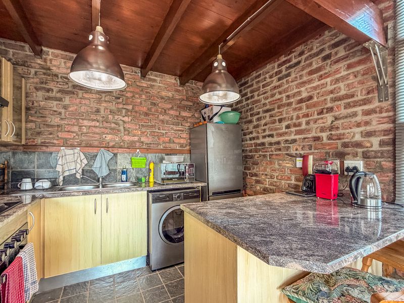 Rustic kitchen featuring exposed brick walls, timber beam ceilings, slate flooring, and functional cabinetry with integrated appliances and a breakfast bar.