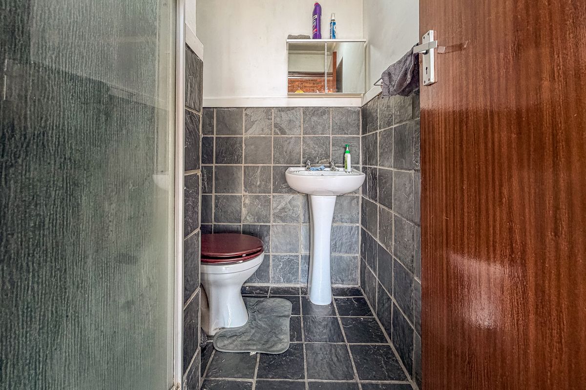 Compact bathroom featuring a pedestal basin, toilet, and shower enclosure with dark slate-style wall and floor tiling.