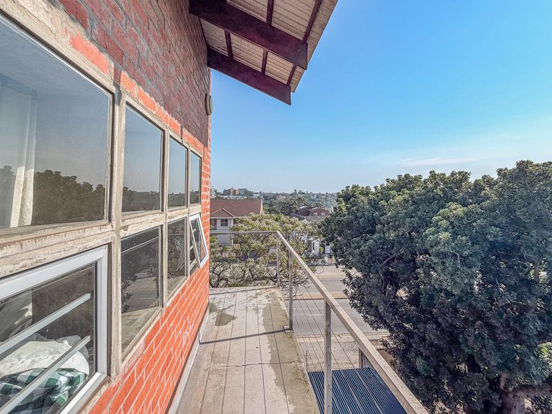 An elevated balcony featuring exposed brickwork, metal railings, and expansive views of the surrounding neighborhood.