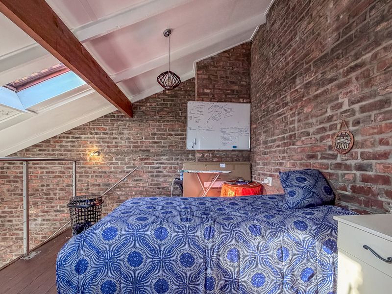 A loft-style bedroom featuring exposed brick walls, timber beams, and a skylight, creating a warm and character-filled living space.