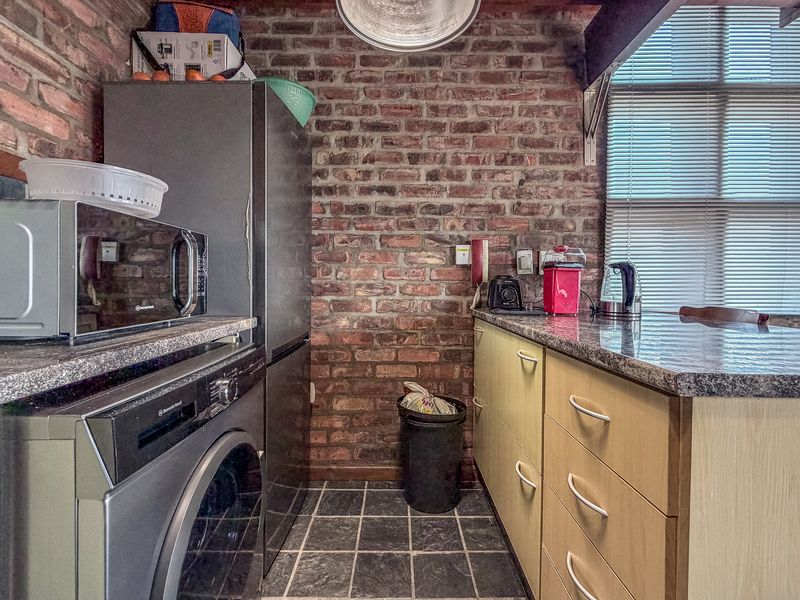 Compact kitchen featuring exposed brick walls, granite countertops, and modern cabinetry, offering a functional and industrial-style workspace.