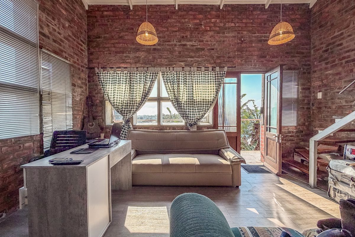A rustic living area featuring exposed brick walls, high ceilings with exposed rafters, and direct access to an outdoor patio area.