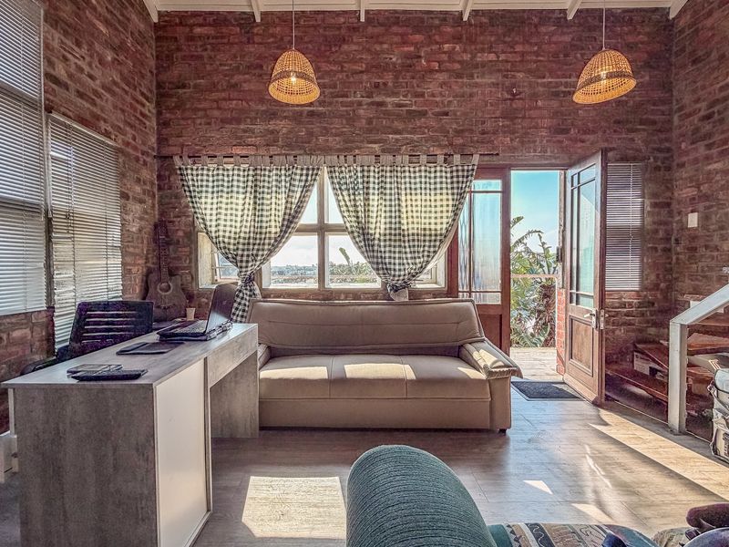 A rustic living area featuring exposed brick walls, high ceilings with exposed rafters, and direct access to an outdoor patio area.