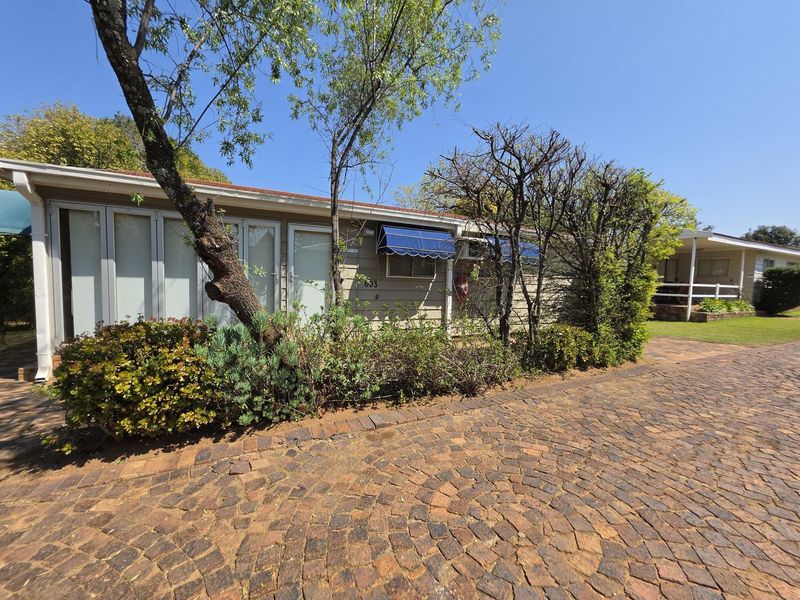 Front exterior view of a single-story residence featuring a cobblestone driveway, folding glass doors, and blue window awnings.