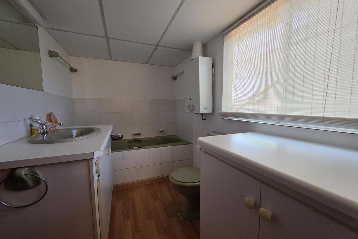 A functional bathroom featuring a built-in vanity, tiled bathtub, toilet, and a wall-mounted gas water heater with a drop ceiling finish.