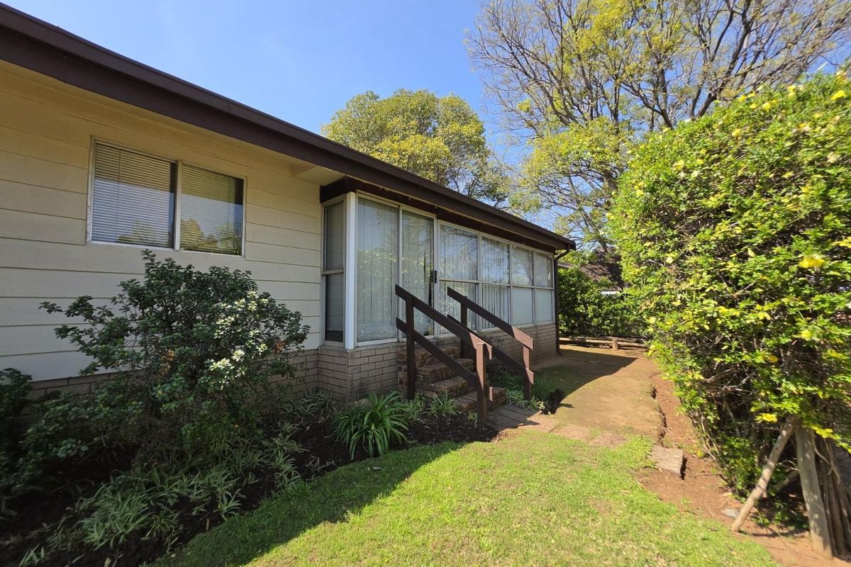 Rear exterior view of the house featuring a concrete pathway, sliding glass doors, and a timber handrail leading to the garden area.