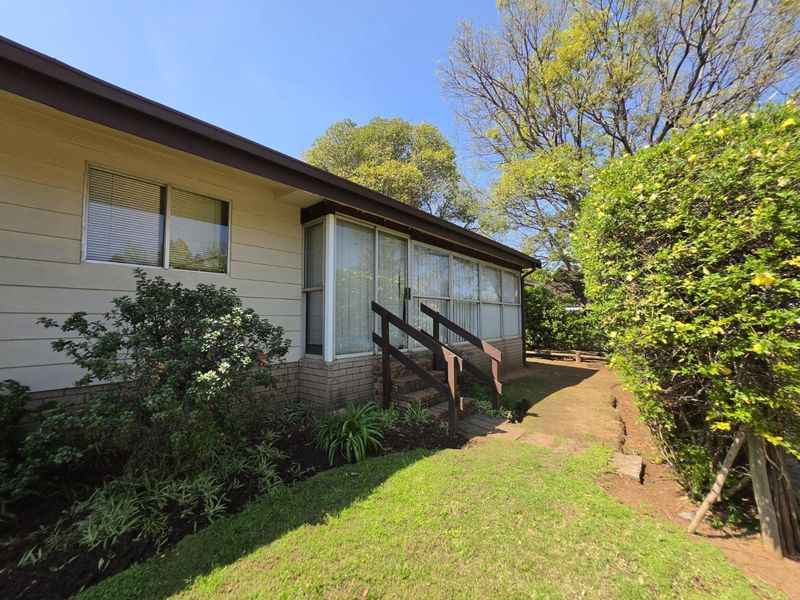 Rear exterior view of the house featuring a concrete pathway, sliding glass doors, and a timber handrail leading to the garden area.