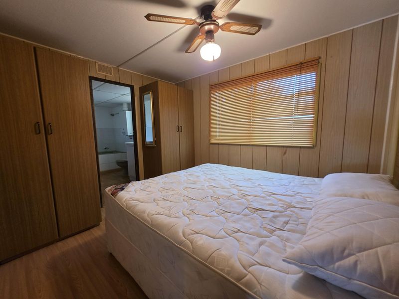 A bedroom featuring built-in wardrobes, wood paneling, and a ceiling fan, with an adjoining bathroom visible through the doorway.