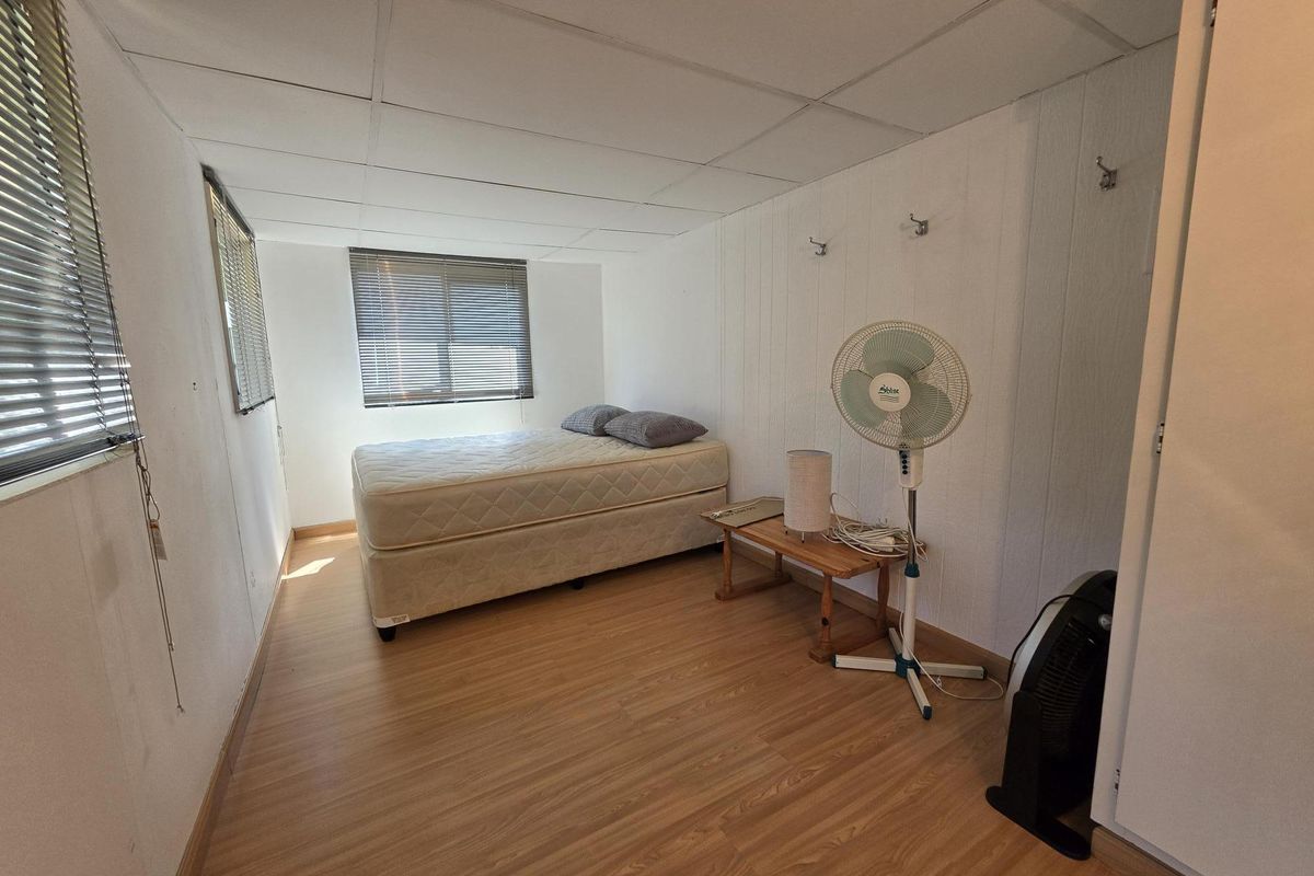 A simple bedroom featuring laminate flooring, a drop ceiling, and multiple windows with venetian blinds.