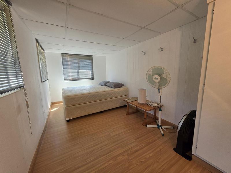 A simple bedroom featuring laminate flooring, a drop ceiling, and multiple windows with venetian blinds.
