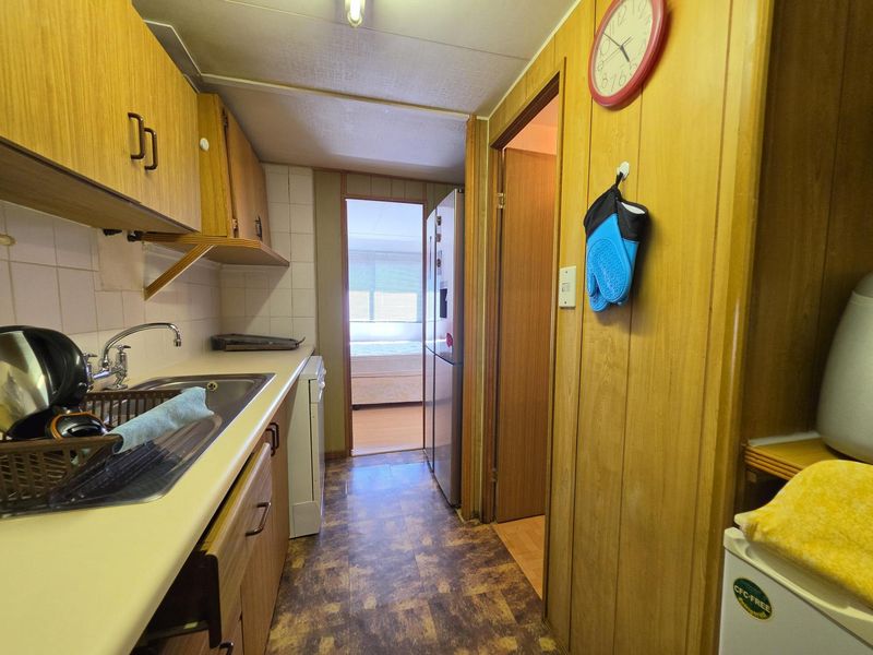A compact kitchen featuring laminate cabinetry, a stainless steel sink, and tiled splashback, with direct access to an adjacent bedroom.