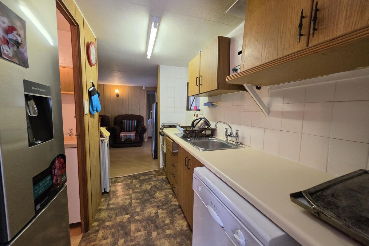 A functional galley-style kitchen featuring laminate cabinetry, tiled splashbacks, and vinyl flooring, leading into an adjacent living area.