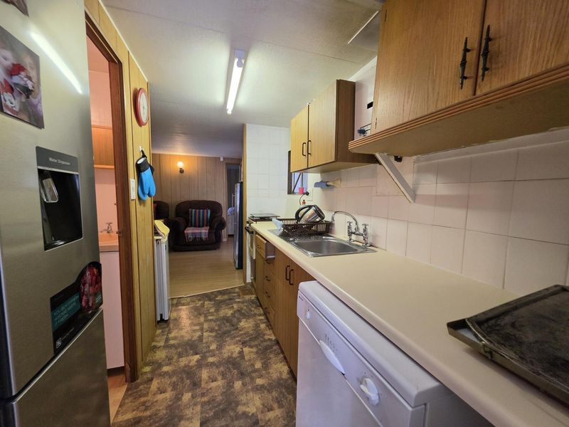 A functional galley-style kitchen featuring laminate cabinetry, tiled splashbacks, and vinyl flooring, leading into an adjacent living area.