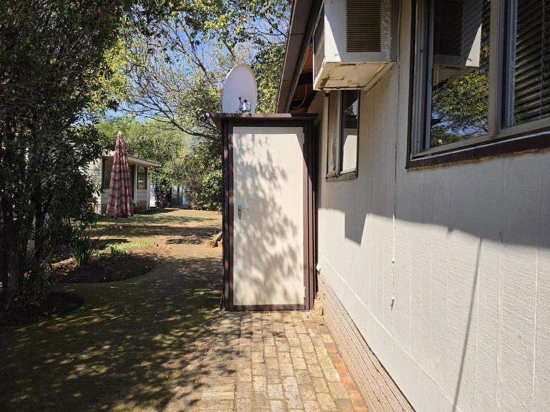 Rear exterior view showing a paved walkway, an external storage unit, and a window-mounted air conditioning unit attached to the house wall.