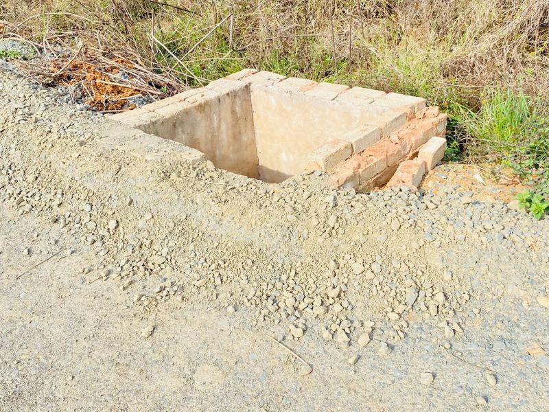 An unfinished brick drainage pit or utility access point located on the edge of the vacant residential land.
