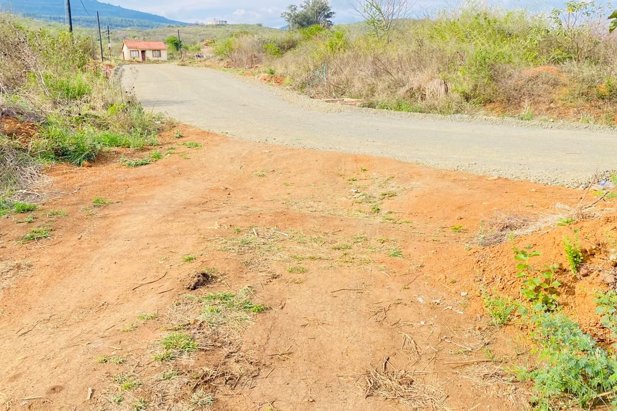 A view of an unpaved access road leading to the residential land, featuring natural terrain and visible utility infrastructure in the surrounding area.