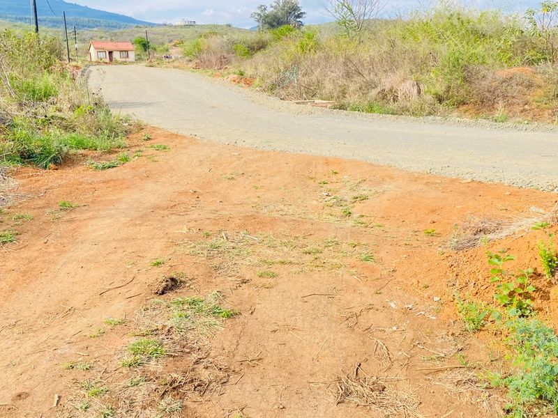 A view of an unpaved access road leading to the residential land, featuring natural terrain and visible utility infrastructure in the surrounding area.