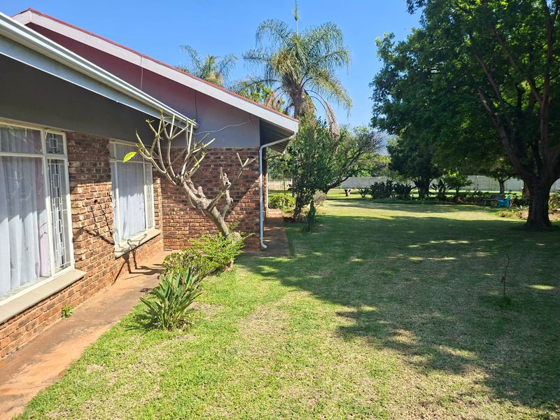 A view of the rear exterior of the house featuring a brick facade, security bars on windows, and a spacious, well-maintained garden.