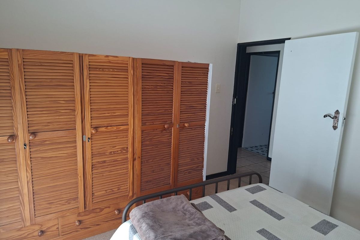 A bedroom featuring built-in wooden louvered wardrobes and access to an adjoining room.