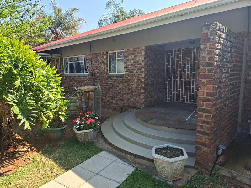 Front entrance of a face brick house featuring a covered porch, concrete steps, and secure metal gate access.