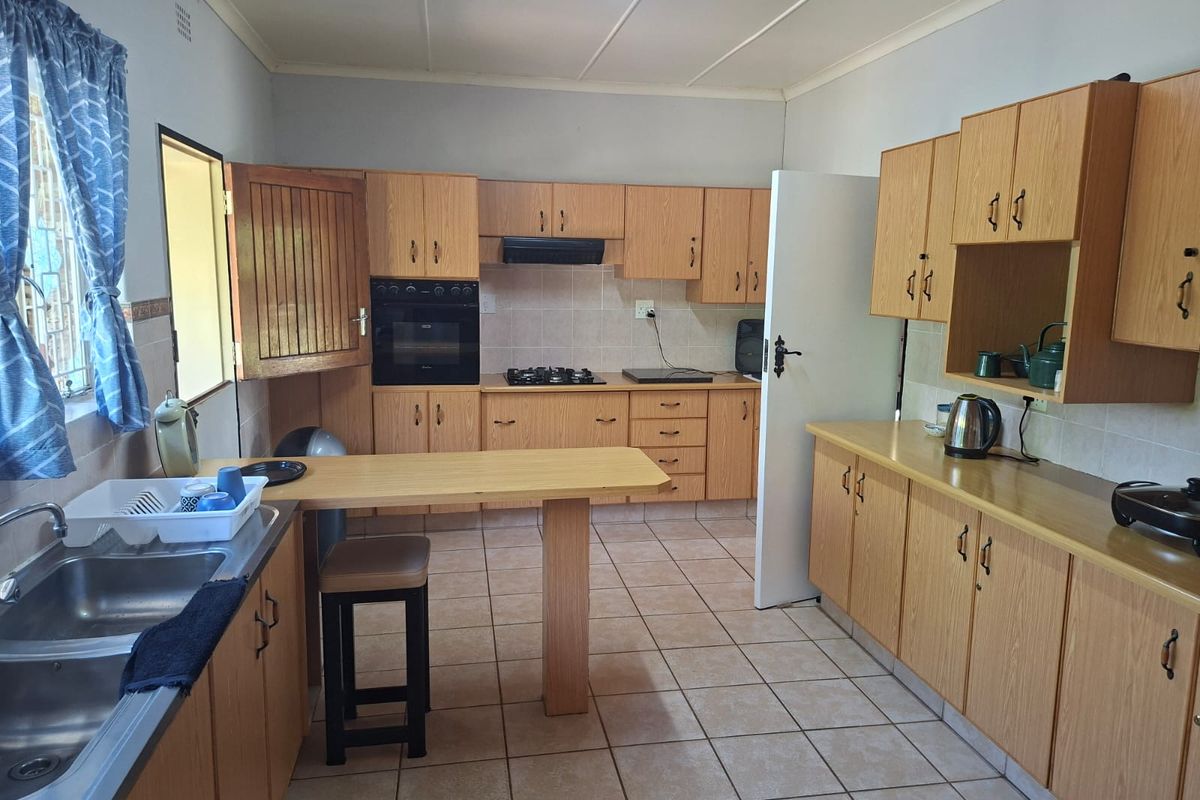 A functional kitchen featuring light wood cabinetry, laminate countertops, a built-in oven, gas hob, and tiled flooring throughout.