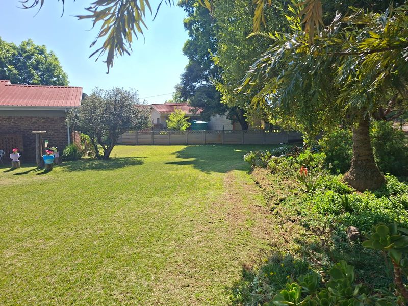 A spacious, well-maintained rear garden featuring a large lawn, mature trees, and established garden beds enclosed by a precast concrete boundary wall.