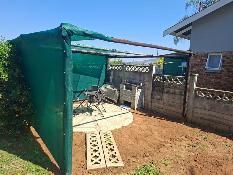 Outdoor patio area featuring a built-in braai, concrete paving, and a shade cloth structure, set within a private garden space.