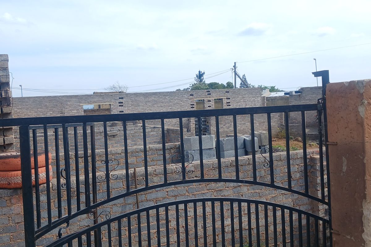 An exterior view of a property under construction, featuring a metal gate and unfinished brick masonry walls.