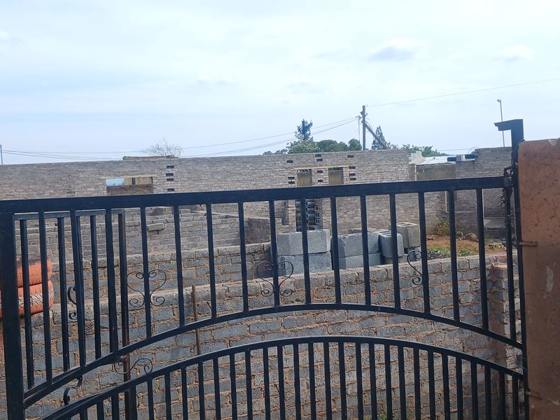 An exterior view of a property under construction, featuring a metal gate and unfinished brick masonry walls.