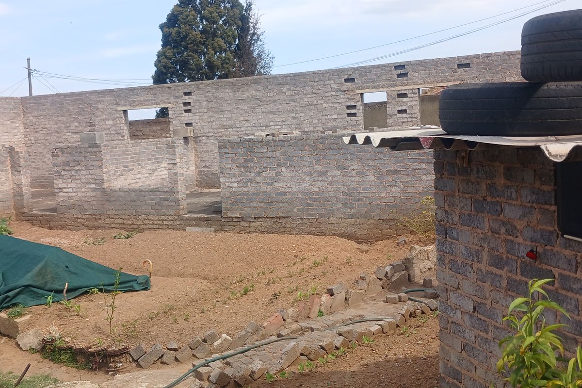 An exterior view of a property under construction, featuring exposed brick walls and incomplete structural elements in a large open yard area.