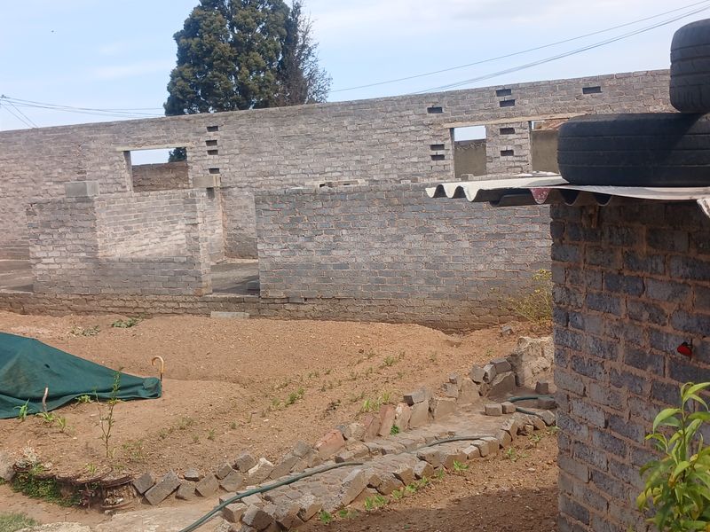 An exterior view of a property under construction, featuring exposed brick walls and incomplete structural elements in a large open yard area.