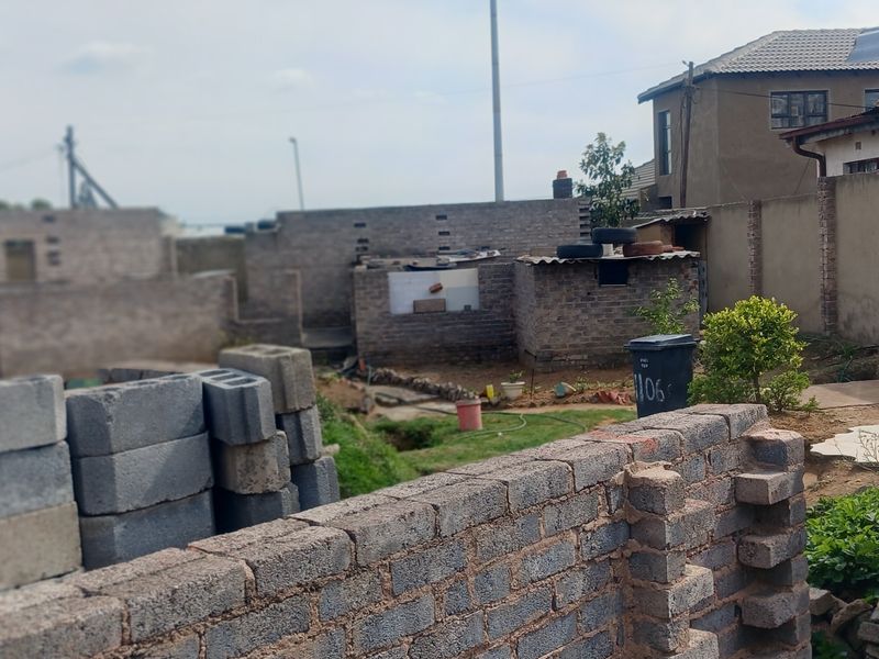Rear yard area featuring unfinished brick boundary walls and a corrugated metal structure in a residential setting.
