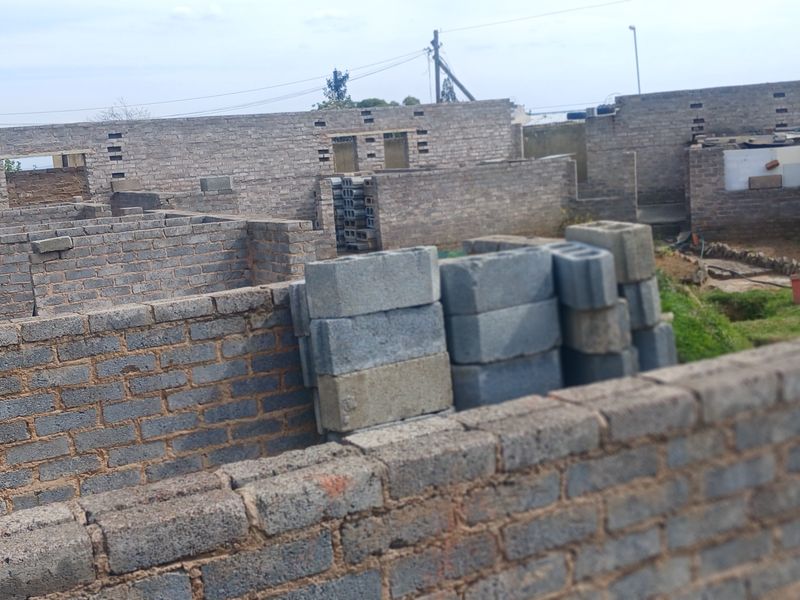 An unfinished construction site showing exposed brick boundary walls and masonry work in progress.