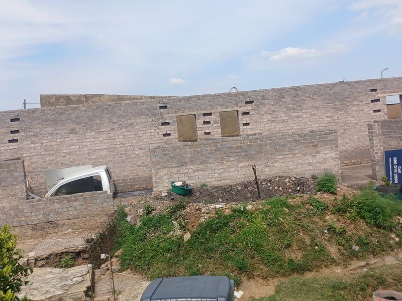 An exterior view of an uncompleted brick structure showing ongoing construction work and an undeveloped rear yard area.